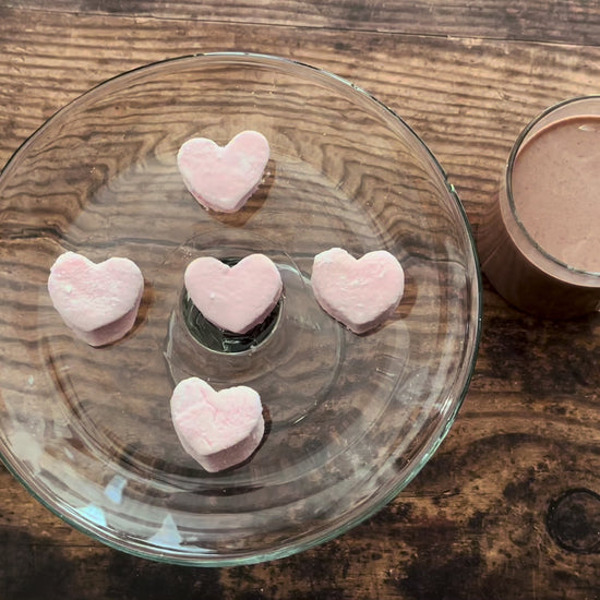 Pink heart-shaped mini marshmallows on a glass plate with a wooden 