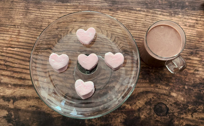 Pink heart-shaped mini marshmallows on a glass plate with a wooden 